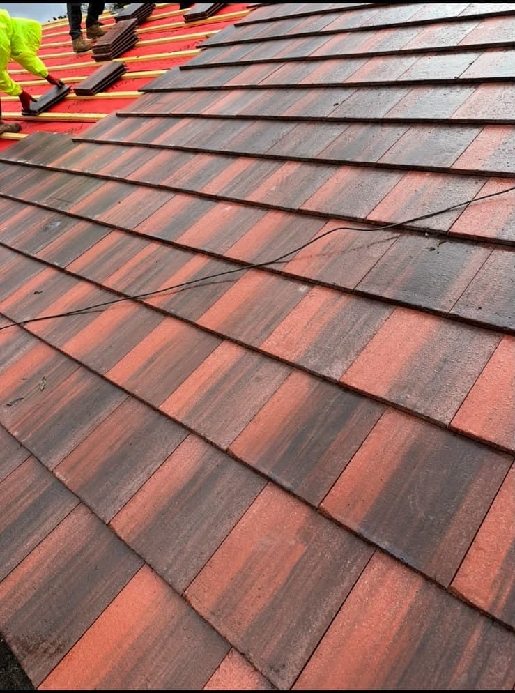 Roofers laying red clay tiles in wet weather