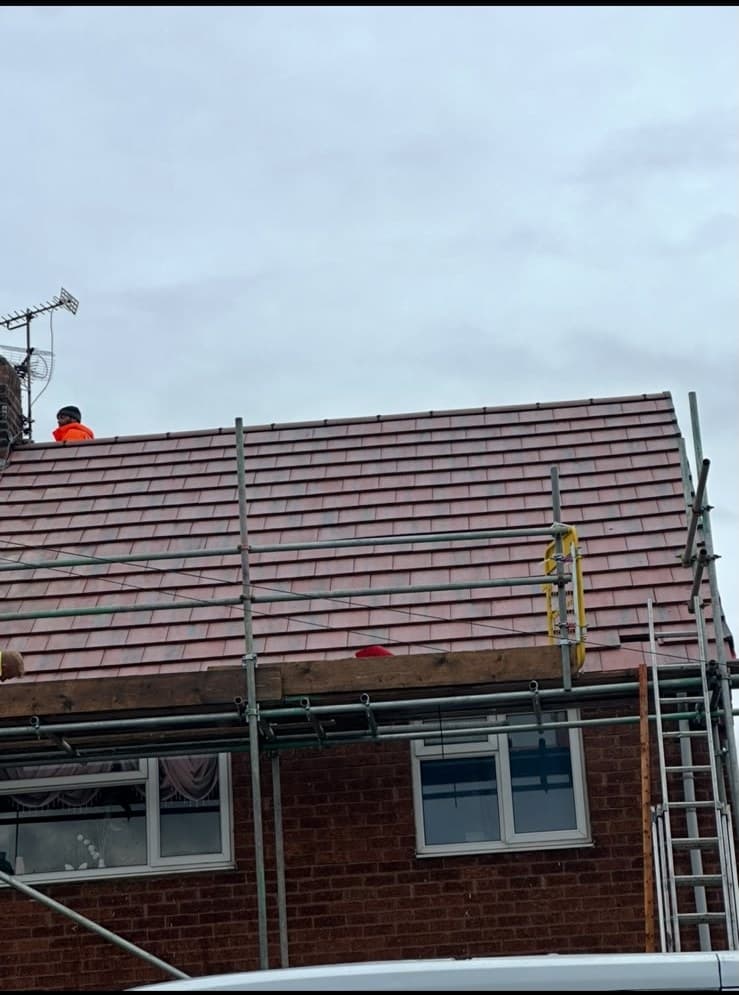 Roofer in hi-vis working on half-tiled roof with scaffolding